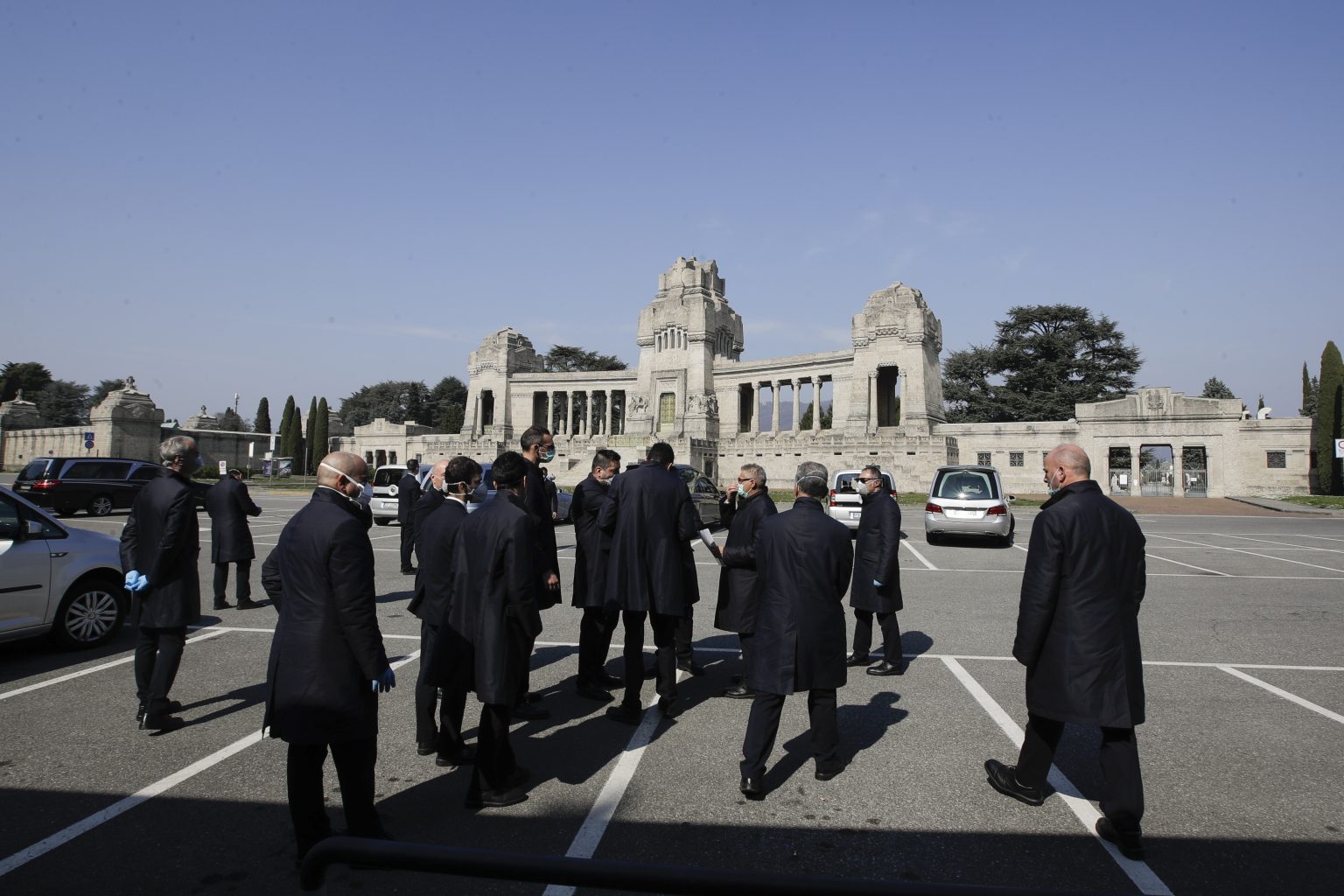 Zamestnanci pohrebnej služby s ochrannými rúškami na tvári vyberajú rakvu z pohrebného auta na cintoríne v severotalianskom meste Bergamo 16. marca 2020. Foto: TASR/AP