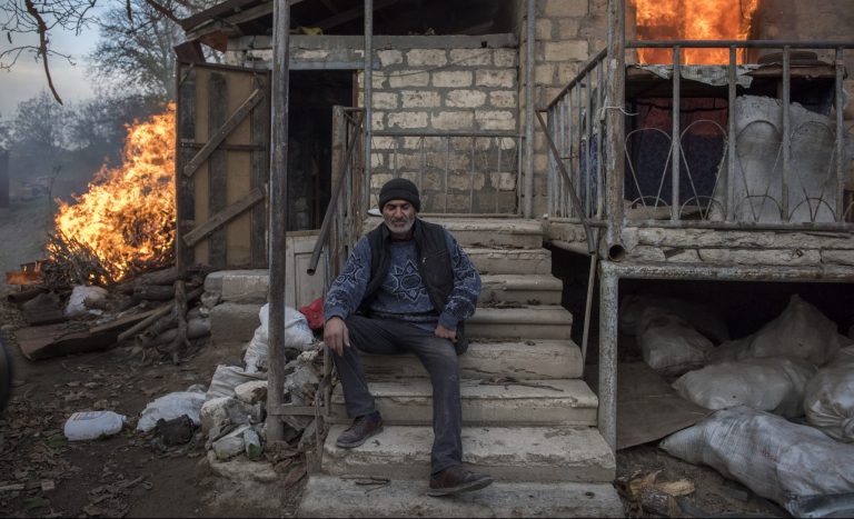 Muž sedí pred horiacim domom v dedine v Náhornom Karabachu. Foto: TASR/AP