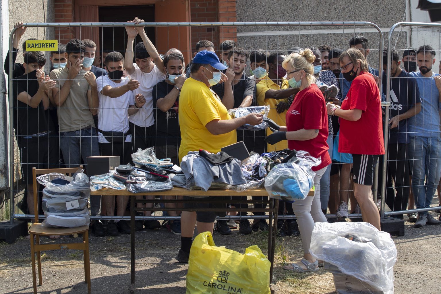 Litovčania rozdávajú veci migrantom, ktorí stoja za plotom v utečeneckom tábore v litovskej dedine Verebiejai. Foto: TAR/AP