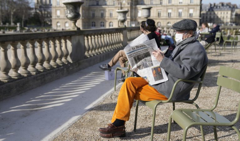 Muž s respirátorom na tvári číta noviny v Luxemburských záhradách v Paríži, v pozadí budova Senátu, hornej komory francúzskeho parlamentu v pondelok 14. marca 2022. Foto: TASR/AP