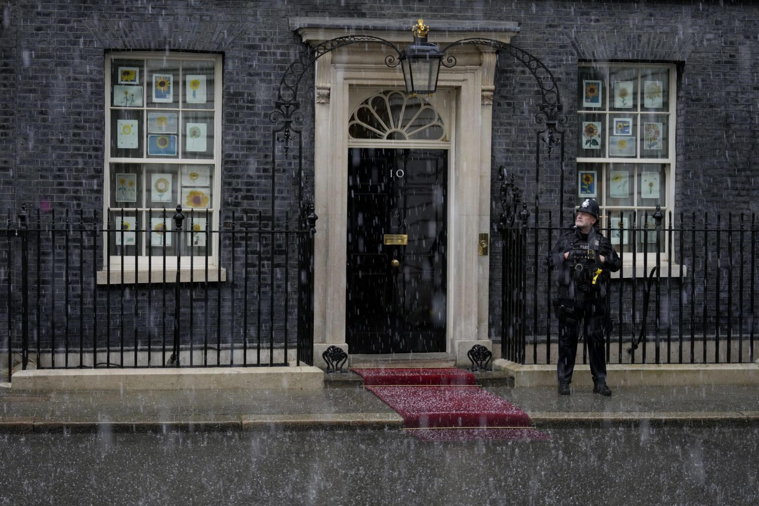 Policajt stojí pred úradom britského premiéra na Downing Street v Londýne počas krupobitia v utorok 24. mája 2022. Foto: TASR/AP