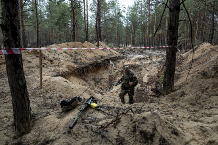 Ukrajinský vojak používa detektor kovov na kontrolu masového hrobu v meste Izium na východe Ukrajiny 15. septembra 2022. Foto: TASR/AP