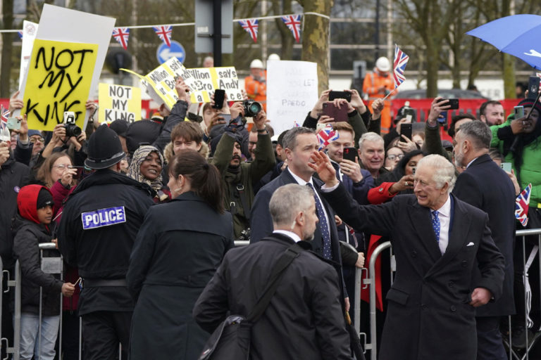 Britský kráľ Karol III máva počas svojej návštevy mesta Milton Keynes vo štvrtok 16. februára 2023, v pozadí protestujúci demonštranti. Foto: TASR/AP