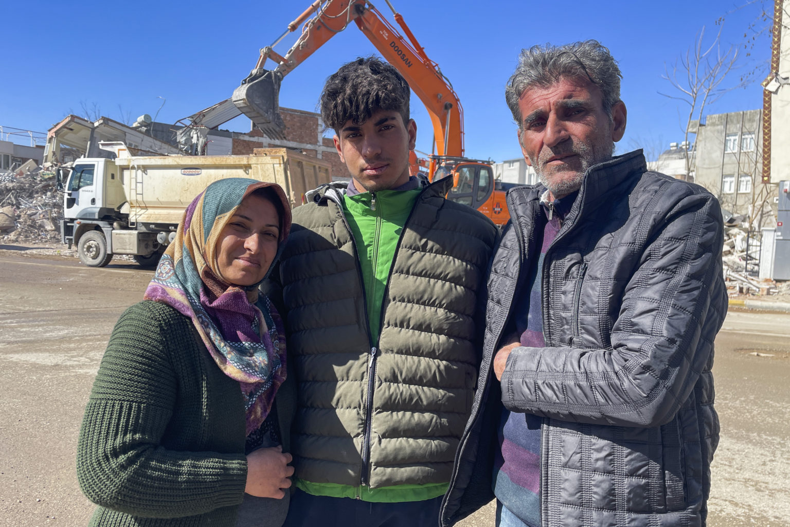 Taha Erdem (17) jeho matka Zeliha Erdemová (37) a otec Ali Erdem (47)  pózujú na fotografii vedľa zničenej budovy, kde bol Tahan zakliesnený po zemetrasení v Turecku. Foto: TASR/AP