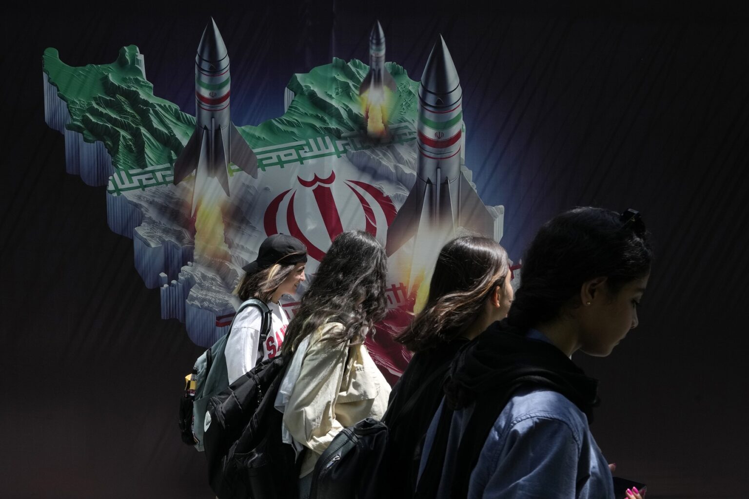 Ženy bez povinnej šatky kráčajú popri plagáte, na ktorom rakety štartujú z mapy Iránu. Foto: Profimedia.sk
