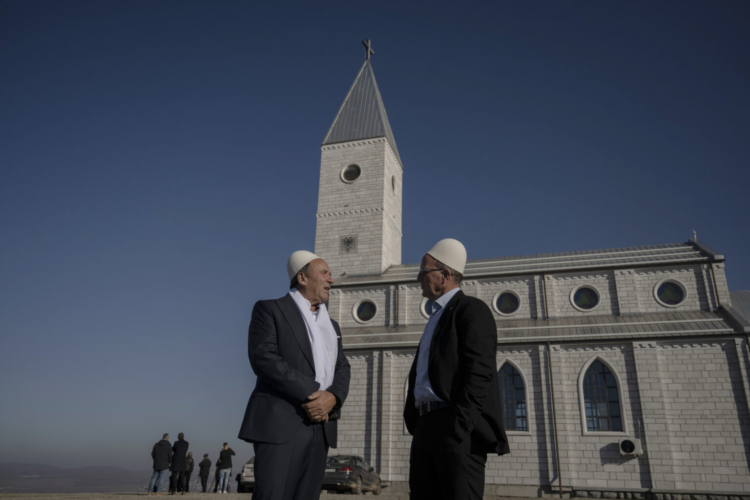 Dvaja muži sa rozprávajú pred kostolom v dedine Llapushnik v Kosove, kde sa v novembri konal obrad krstu. Foto: Armend Nimani pre New York Times