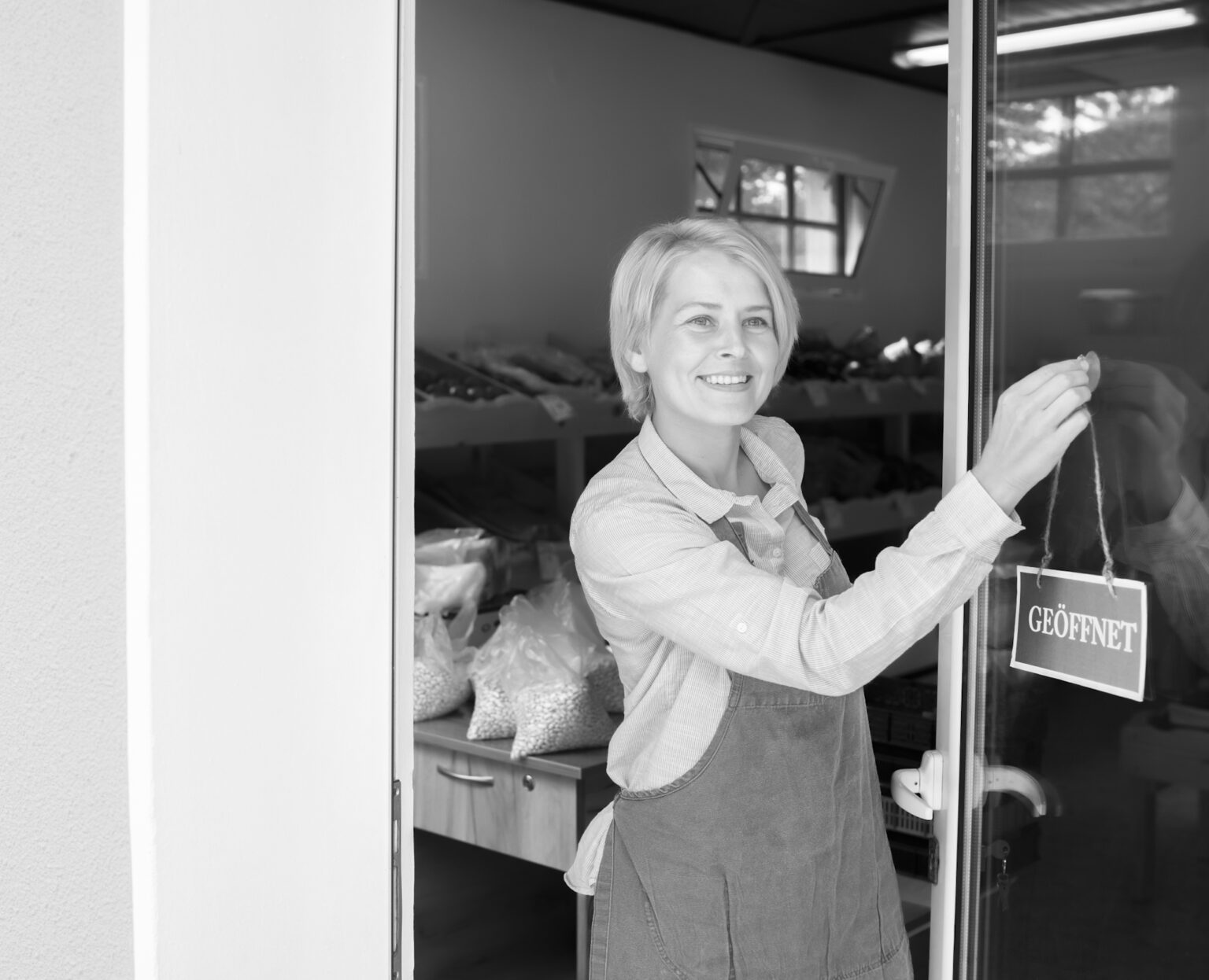 A woman with apron hanging an open sign on the window of her shop. Photo: Vladimir Vladimirov / Getty Images