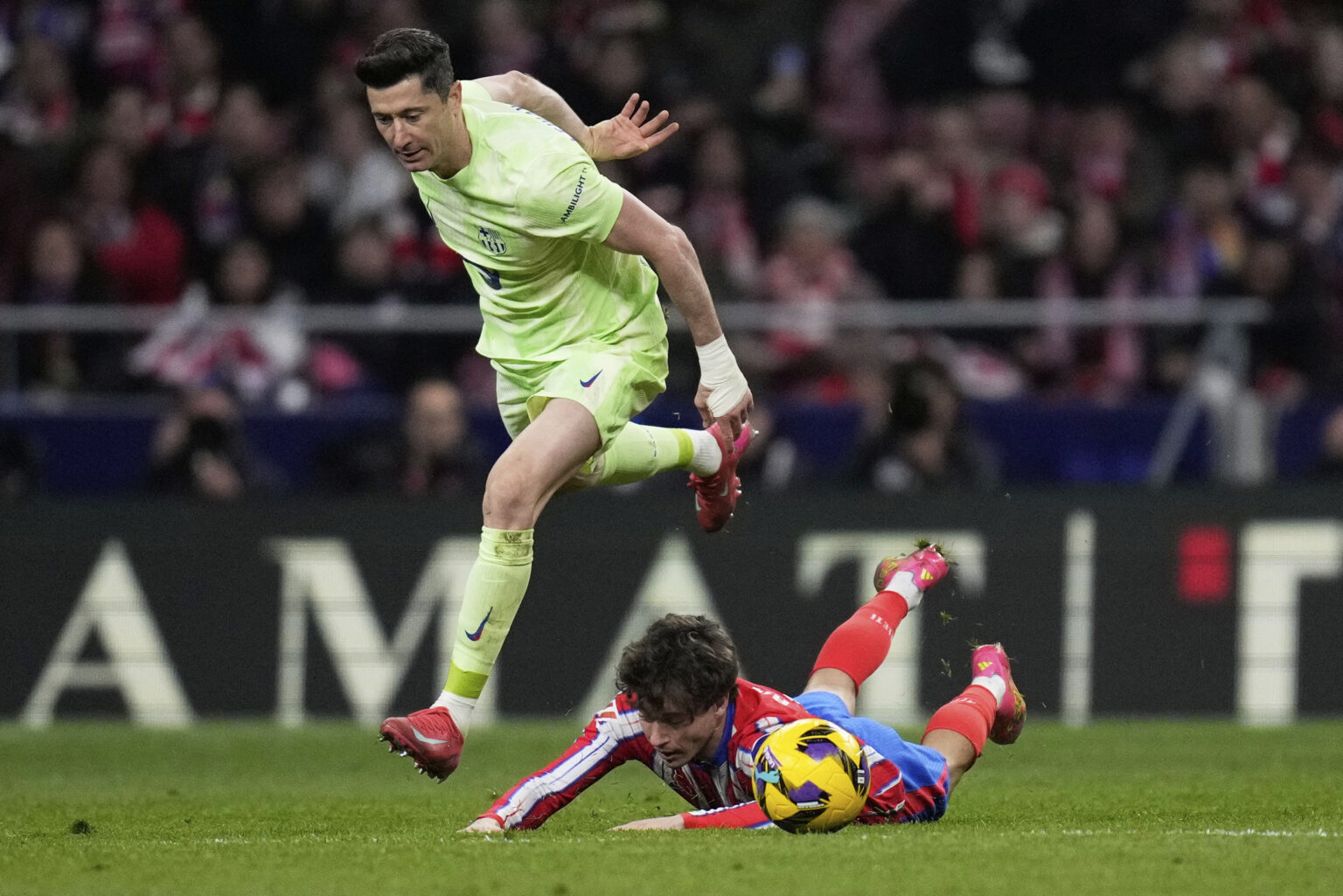 Robert Lewandowski preskakuje Rodriga Riquelmeho z Atletica počas zápasu 16. marca 2025. Foto: AP Photo/Bernat Armangue