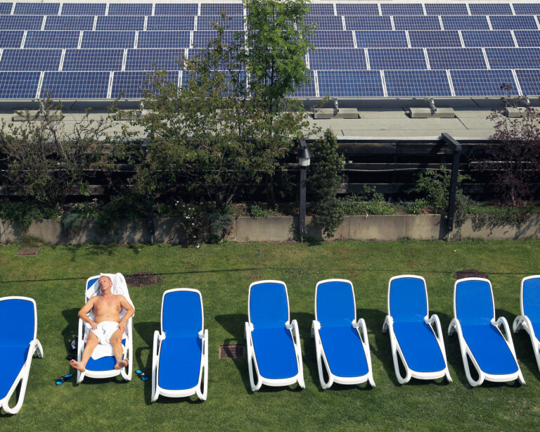 Muž sa opaľuje na streche vedľa solárnych panelov. Berlín, Nemecko. Foto: Sean Gallup/Getty Images