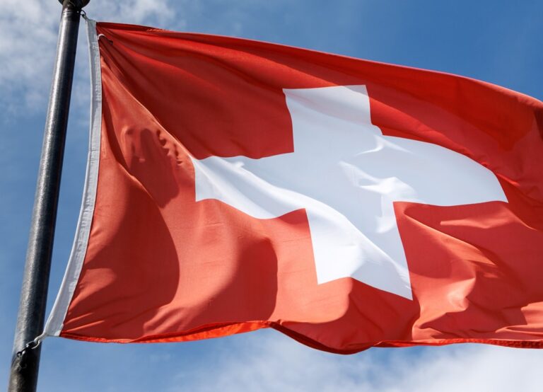 Switzerland, Schaffhausen: A rectangular flag of Switzerland (Schwiz, Suisse, Helvetia, Swiss Confederation) flies in the wind on a flagpole in Schaffhausen (Canton of Schaffhausen, Switzerland) against the blue sky. Switzerland is a federalist, democratic state in Europe. The Swiss flag shows a white Swiss cross on a red background. Photo: Matthias Balk/dpa (Photo by Matthias Balk/picture alliance via Getty Images)