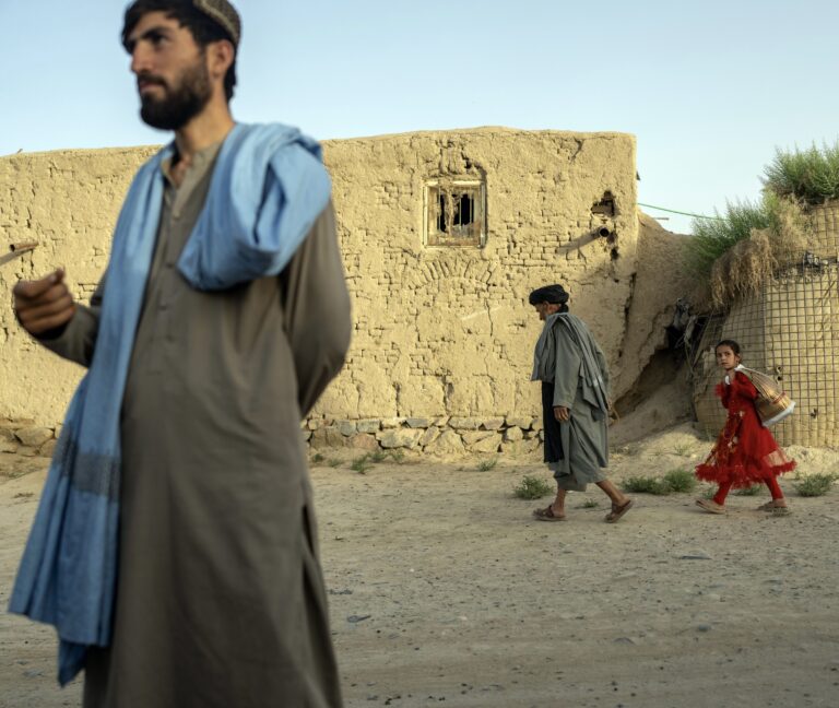 Muž a dievča prechádzajú okolo starých bariér Hesco, ktoré sa počas vojny používali na ochranu pred streľbou z ručných zbraní alebo výbuchmi, v dedine Deh-e Kuchay v Afganistane 10. mája 2025. Foto: João Silva/New York Times