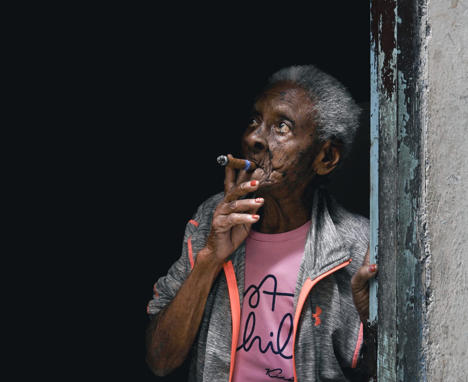 Staršia žena fajčí cigaru na prahu svojho domu v Havane. Foto: Norlys Perez/ Reuters