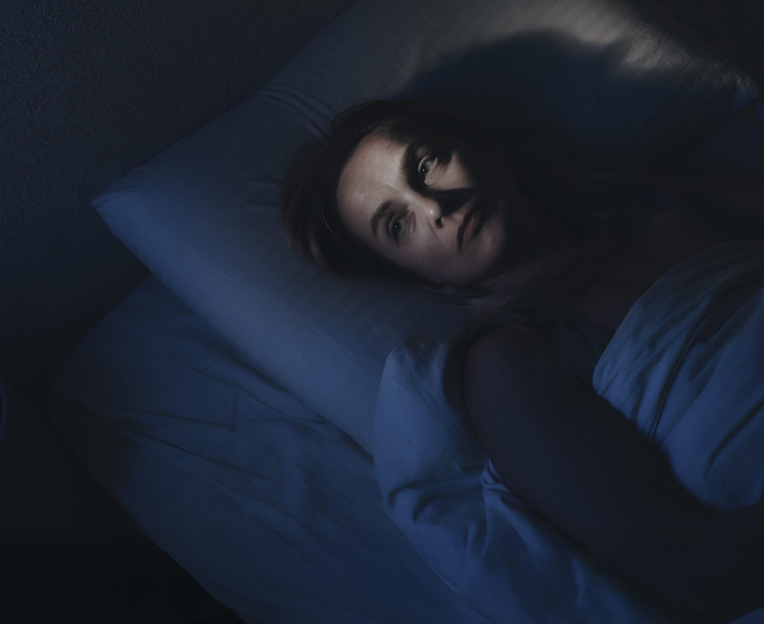A woman lies awake in bed, unable to fall asleep, a common experience in a 24/7 world. Photo: Ekaterina Goncharova / Getty Images