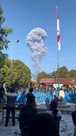 People watch smoke rising after the eruption of Mount Dukono.