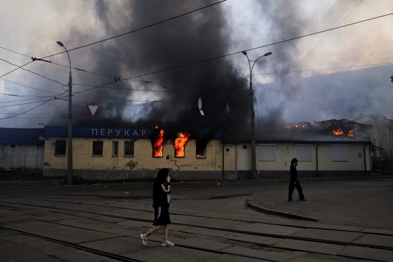 Ľudia prechádzajú okolo horiacej budovy v Kyjeve.