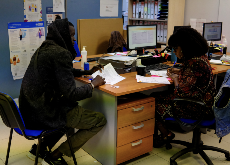Zamestnanec pomáha migrantovi z Afriky s formulármi.