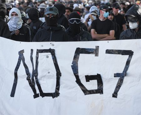 Protesters carry a banner reading “No G7”.