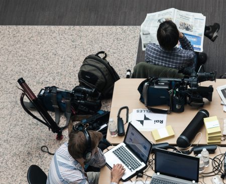 Journalists read newspapers and work on laptops.