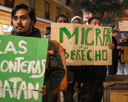 A migrant from Africa holds a sign saying 'migration is a right'.