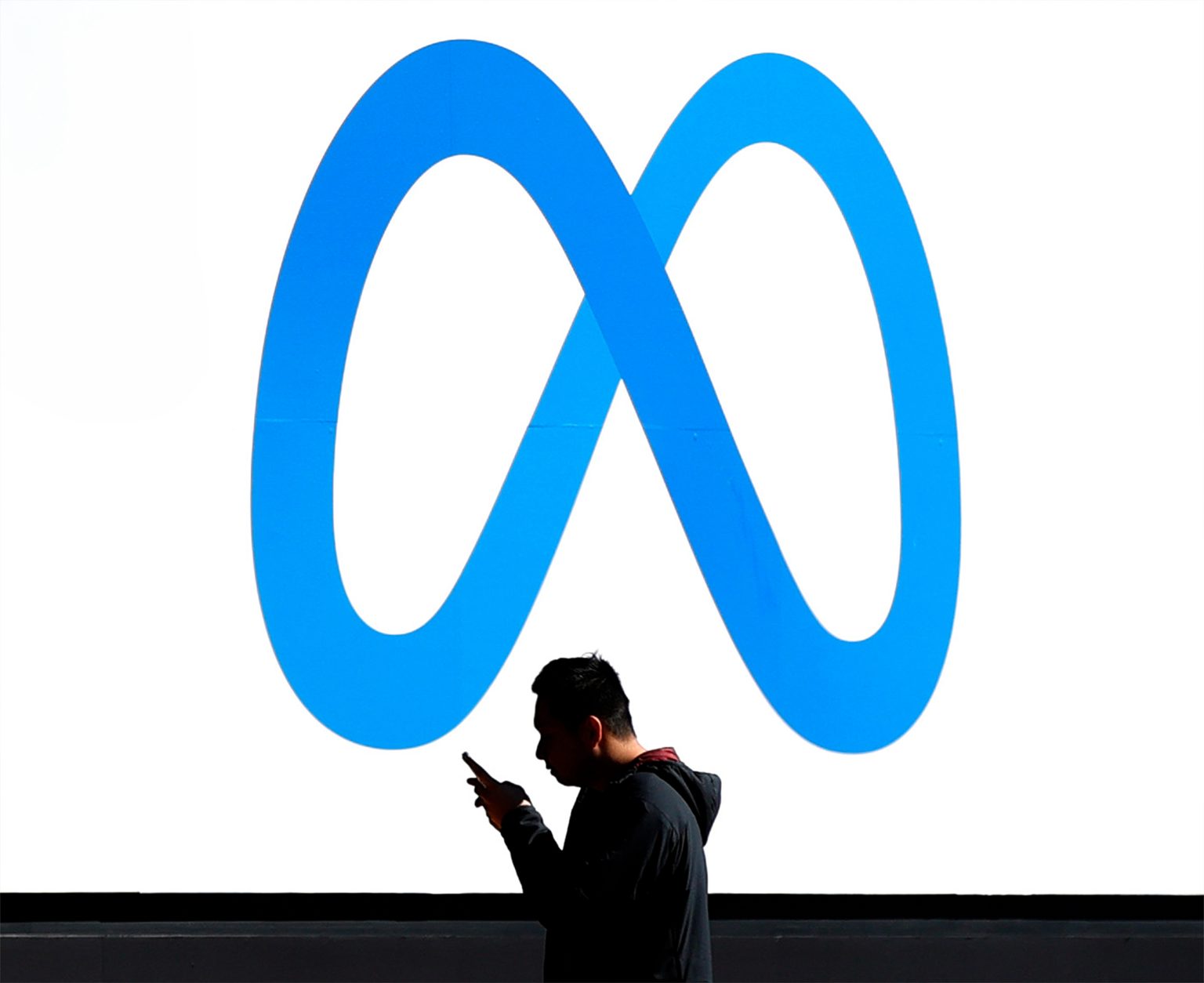 A pedestrian walks in front of a new logo and the name 'Meta' on the sign in front of Facebook headquarters. Photo: Justin Sullivan/Getty Images