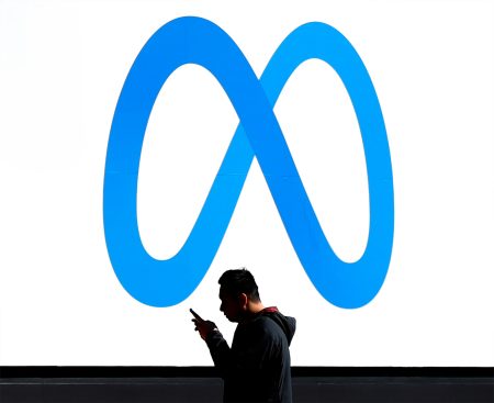A pedestrian in front of the Meta logo at Facebook headquarters.