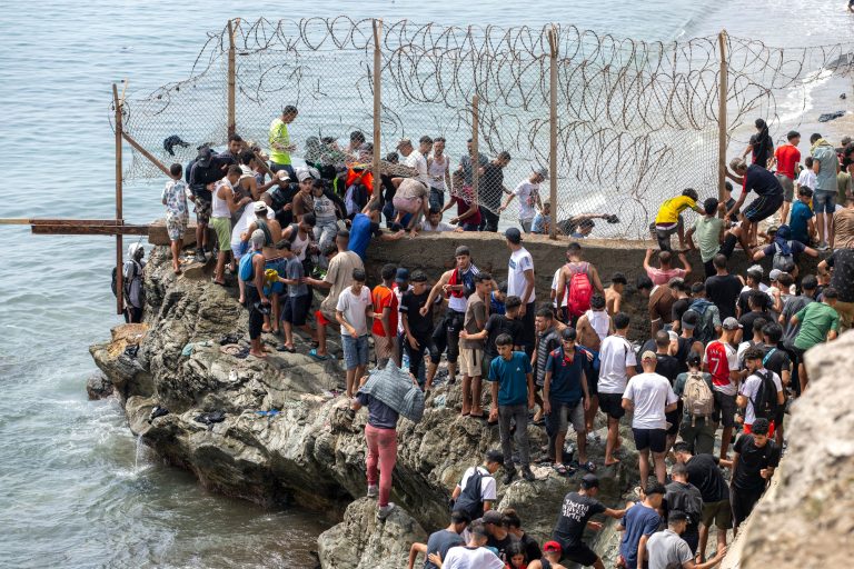 Migranti prechádzajú cez ostnatý drôt na hranici.